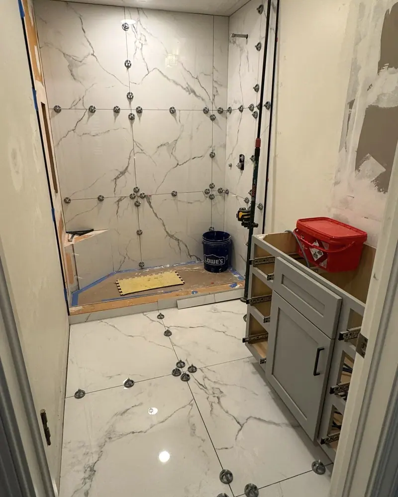 Large marble-look porcelain tile being set on shower walls and floor with leveling clips
