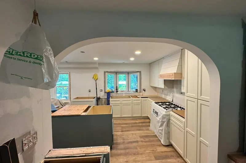 Kitchen seen through an arched opening while new cabinets go in