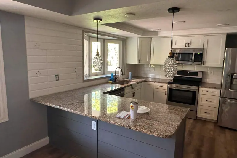 Granite peninsula on a gray shiplap base under glass pendants