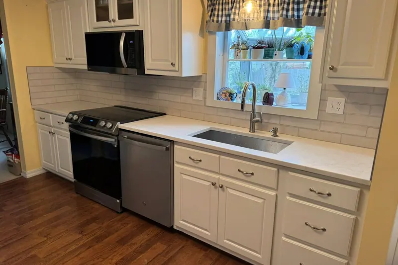 White kitchen with white quartz counters and subway tile around the window over the sink