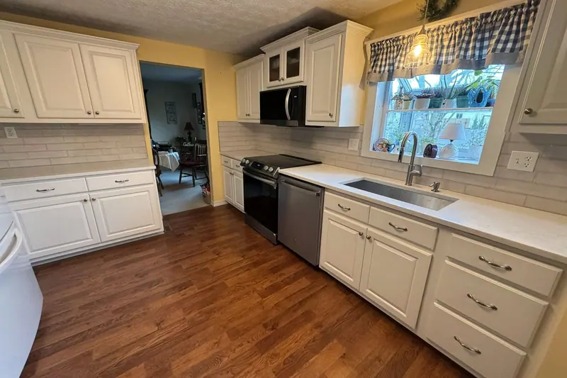 White kitchen with subway tile, a window over the sink and wood floors