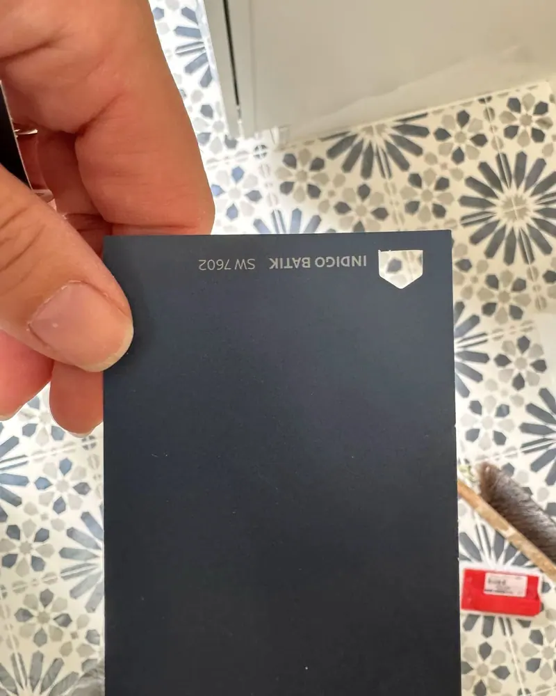 A dark blue paint swatch held against patterned floor tile while choosing a laundry room color